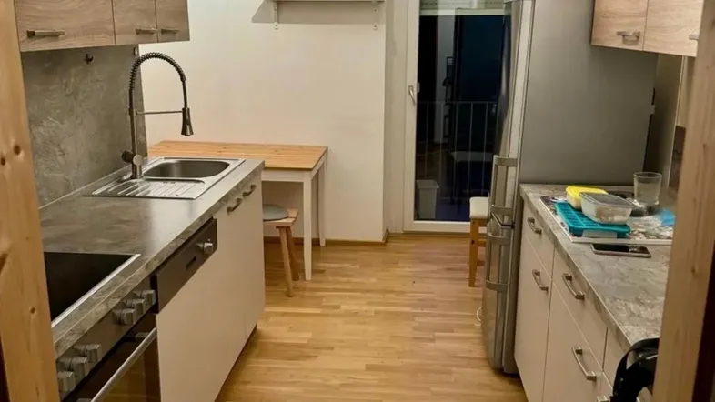 Moderne Küche mit Holzschränken, grauer Arbeitsplatte und Zugang zum Balkon.