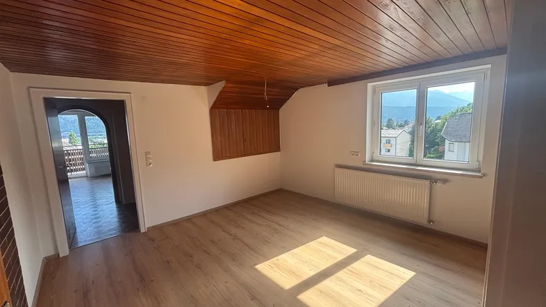 Helles Zimmer mit Holzbalkendecke, Laminatboden und Fensterblick auf die Berge.