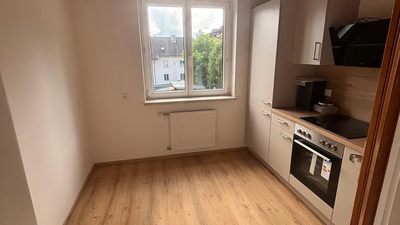 Kleine Küche mit weißen Schränken, integriertem Backofen und Induktionskochfeld, dazu eine Holzdecke.