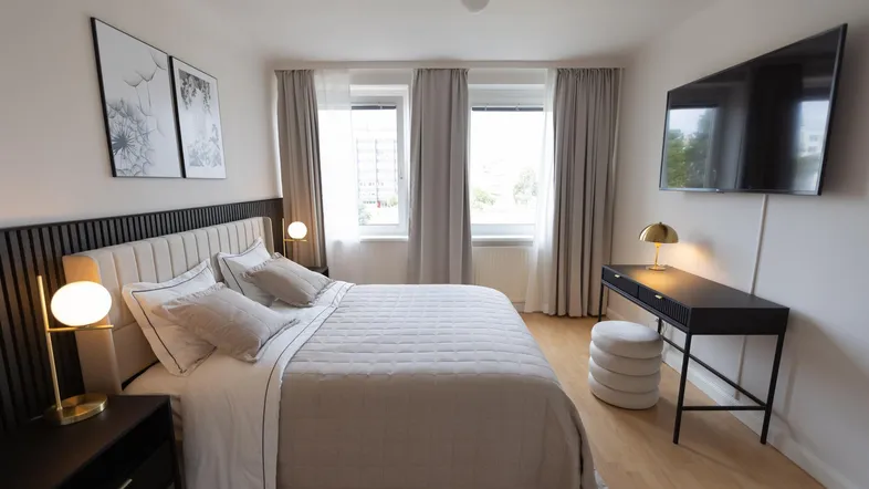 Modernes Schlafzimmer mit beigem Polsterbett, dunklen Nachttischen und einem Schreibtisch.
