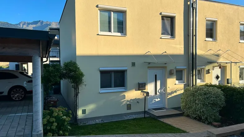 Modernes Reihenhaus mit heller Fassade, Carport und gepflegtem Vorgarten in sonniger Lage.