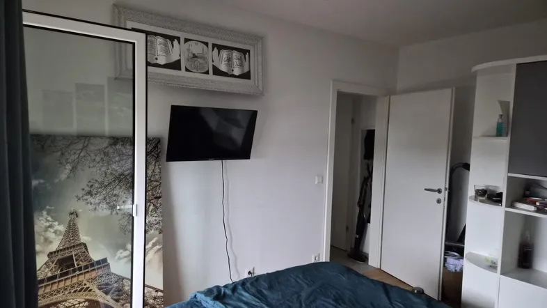 Schlafzimmer mit Doppelbett, Wandfernseher und Schrank mit Eiffelturm-Motiv.