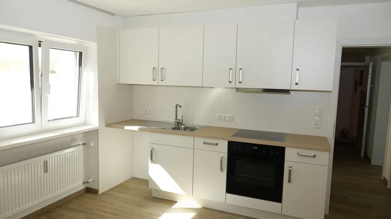 Helle, moderne Küche mit weißen Schränken, Holzarbeitsplatte und Fenster für natürliches Licht.