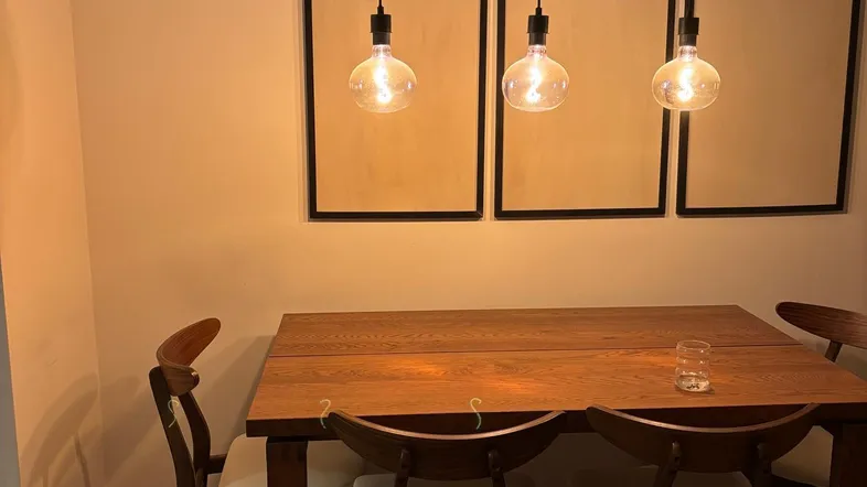 Gemütlicher Essbereich mit Holztisch, modernen Pendelleuchten und dekorativen Wandrahmen.