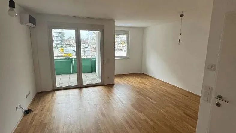 Helles Wohnzimmer mit Parkettboden und Zugang zu einem Balkon, ideal für entspannte Stunden.