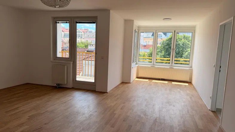 Weitläufiges Wohnzimmer mit Eichenparkett, großen Fenstern und Zugang zu einem französischen Balkon.