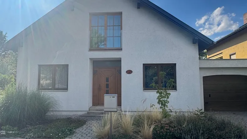 Weißes Einfamilienhaus mit Satteldach, brauner Eingangstür und integrierter Garage unter blauem Himmel.