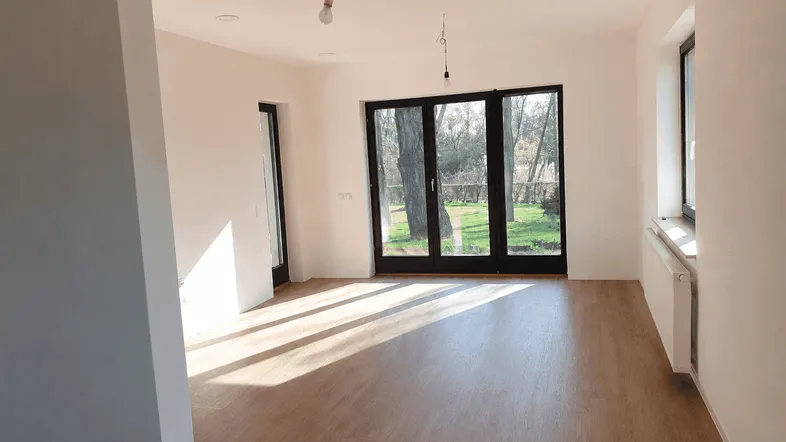 Heller Wohnraum mit großen Fenstern, Laminatboden und direktem Zugang zum Garten.