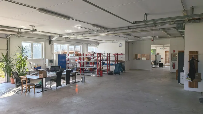 Großer offener Lagerbereich mit Betonboden, vielen Fenstern und Arbeitsplätzen, ideal für gewerbliche Nutzung.