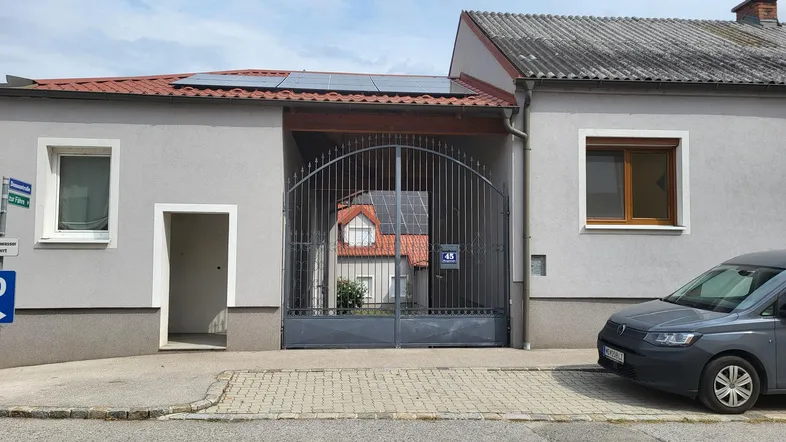 Fassade eines Wohnhauses mit großem Metalltor, Solaranlage auf dem Dach und einem geparkten Auto davor.