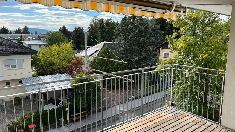 Geräumiger Balkon mit Holzboden, Metallgeländer und Markise, bietet einen weiten Blick ins Grüne.