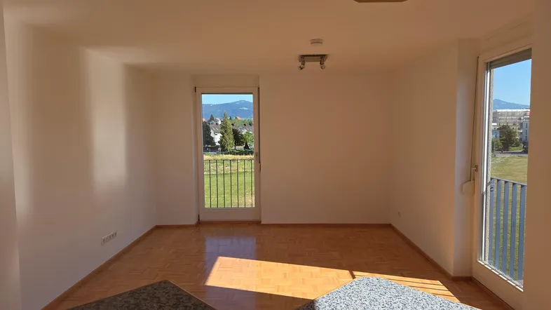 Helles Wohnzimmer mit Parkettboden und Zugang zum Balkon, bietet einen weiten Blick ins Grüne.