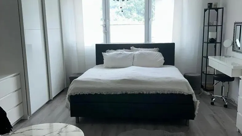 Helles Schlafzimmer mit modernem Bett, weißen Kleiderschränken und einem Schminktisch am Fenster.