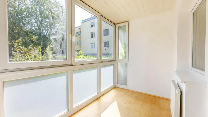 Helle verglaste Loggia mit Holzboden und Blick ins Grüne, ideal zum Entspannen.