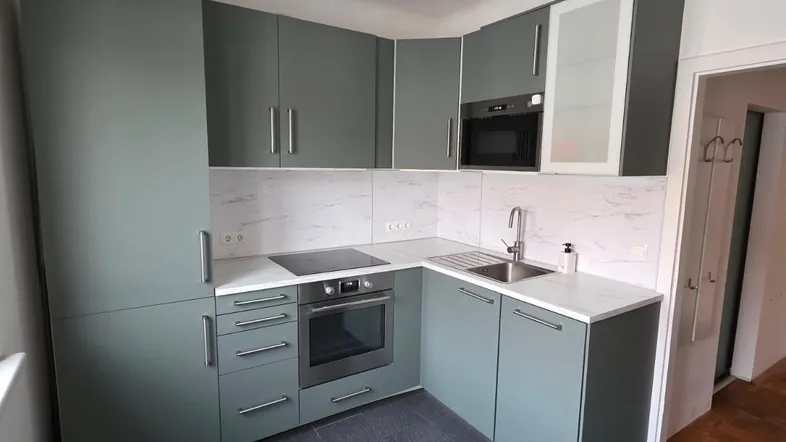 Moderne Küche in Grüntönen mit integrierten Geräten, dunklem Fliesenboden und heller Arbeitsplatte.