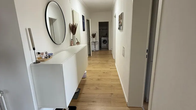 Heller Flur mit modernem Konsolentisch, Spiegel und durchgehendem Holzfußboden.