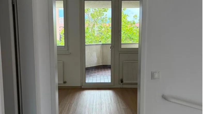 Heller Flur mit Holzfußboden und direktem Zugang zu einem sonnigen Balkon mit grüner Aussicht.
