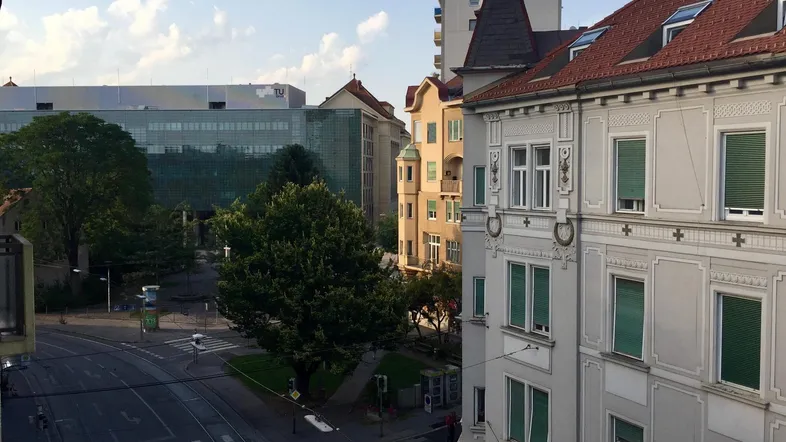 Blick auf eine belebte Stadtstraße mit historischen und modernen Gebäuden sowie Bäumen.