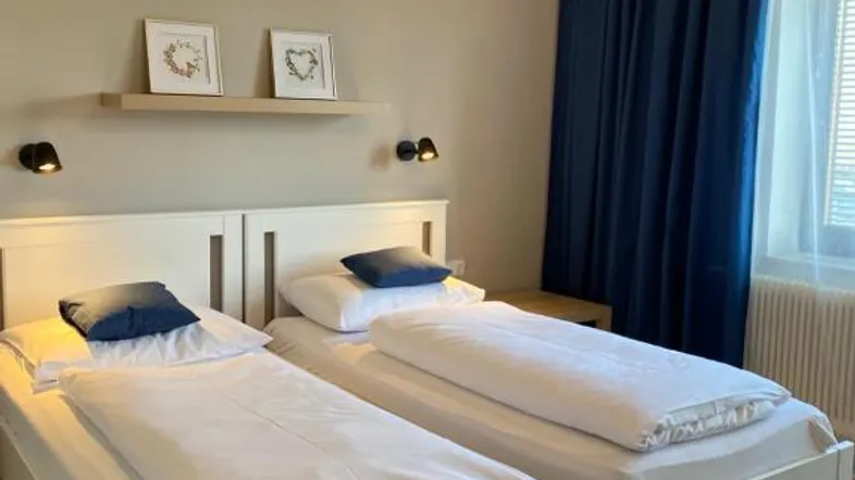 Helles Schlafzimmer mit zwei Einzelbetten, beigen Wänden und blauen Vorhängen für eine gemütliche Atmosphäre.