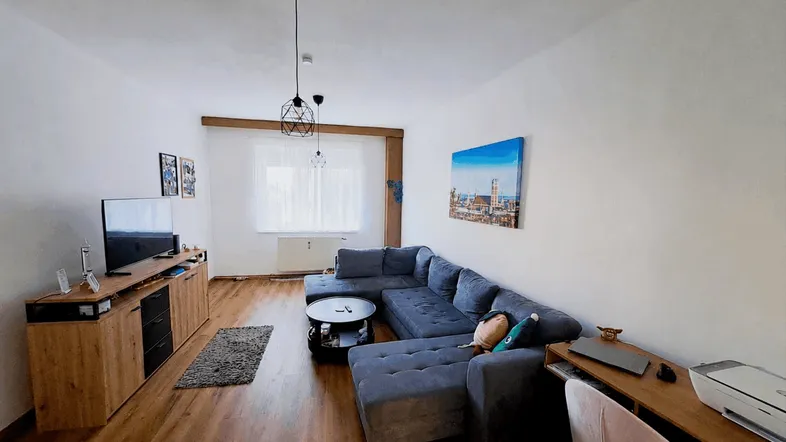 Helles Wohnzimmer mit großem Ecksofa, Holzboden und einem Arbeitsbereich am Fenster.