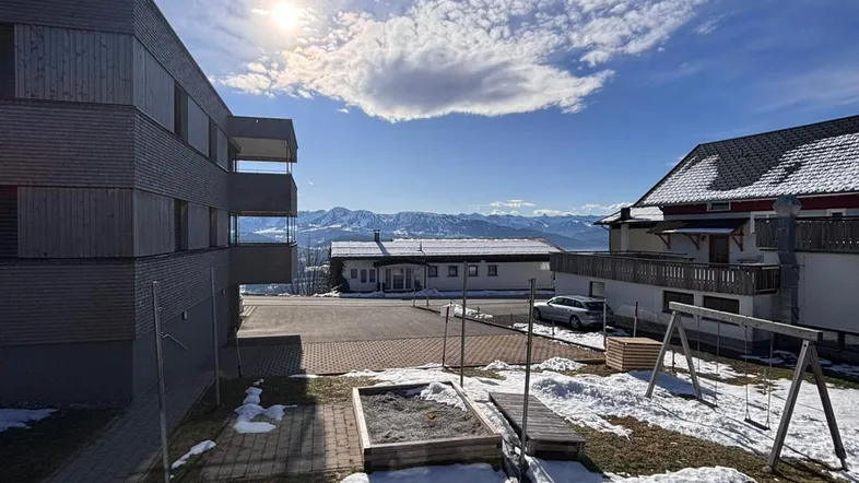 Außenbereich mit Spielplatz, Neubau und Panoramablick auf die Berge im Winter.