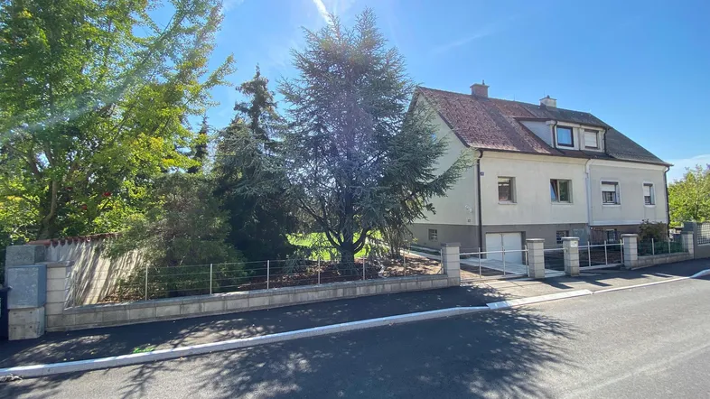 Vorderansicht eines Hauses mit gepflegtem Vorgarten, Einfahrtstor und sonnigem Wetter.