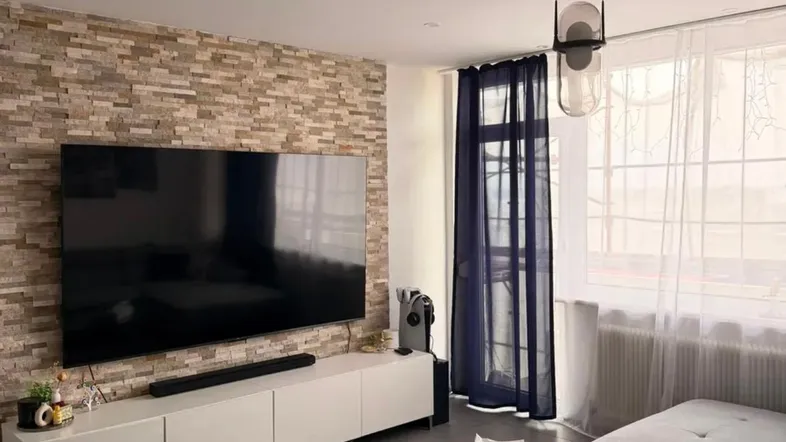 Modernes Wohnzimmer mit Steinwand, großem Fernseher und bequemer Eckcouch.