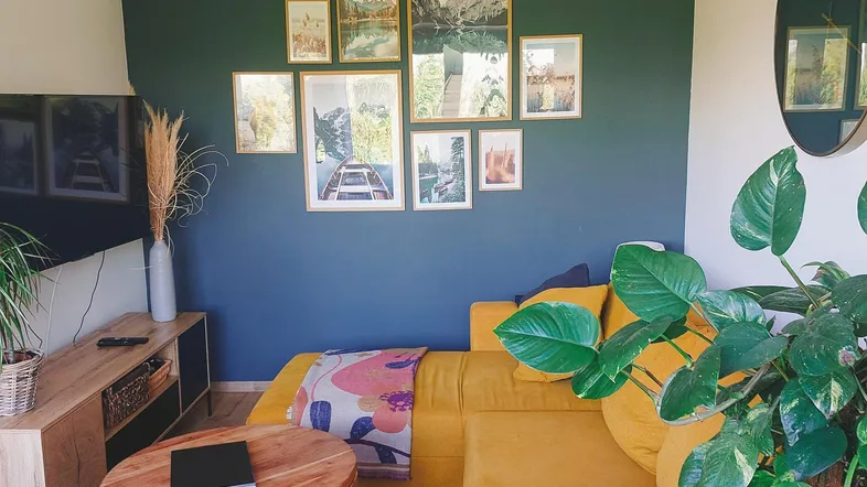 Helles Wohnzimmer mit gelbem Sofa, dunkler Akzentwand und Holztisch.