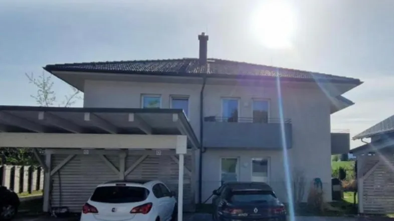 Modernes Wohnhaus mit Carport und Satteldach unter strahlendem Sonnenschein.