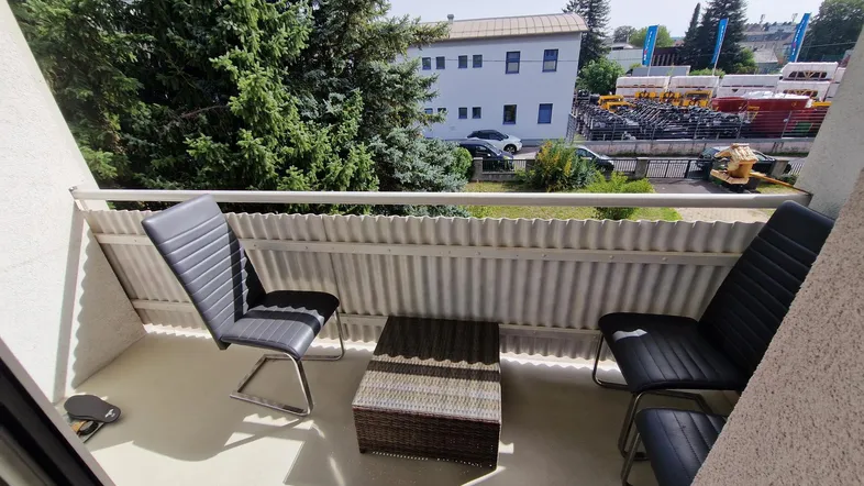 Kleiner Balkon mit Sitzgelegenheiten und Blick auf die umliegenden Gebäude und Bäume.