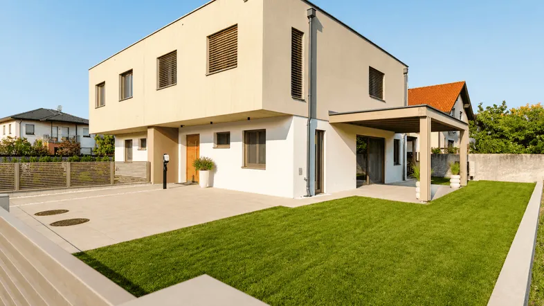 Modernes Einfamilienhaus mit heller Fassade, gepflegtem Rasen und gepflastertem Vorplatz.