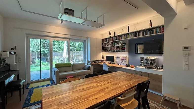 Geräumiger Wohn- und Essbereich mit großem Holztisch, Sofa und direktem Zugang zum Garten.
