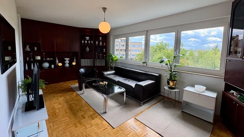 Helles Wohnzimmer mit Parkettboden, dunklen Holzmöbeln und Blick ins Grüne.