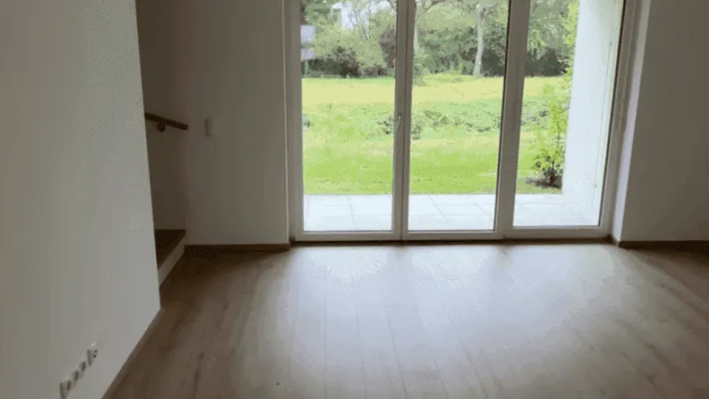 Helles Wohnzimmer mit Laminatboden und großen Fenstern mit Blick ins Grüne.