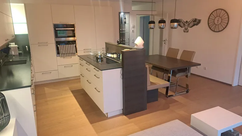 Offener Wohn- und Essbereich mit moderner Einbauküche, Kücheninsel und hellem Parkettboden.