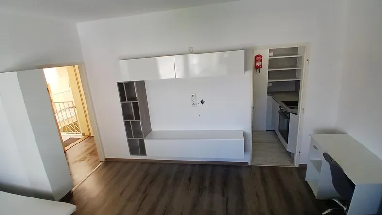 Helles Wohnzimmer mit modernem TV-Möbel, Schreibtisch und Zugang zu einer kleinen Küche.