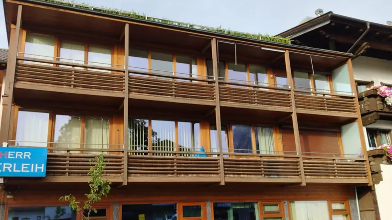 Mehrstöckiges Gebäude mit Holzfassade und mehreren Balkonen, umgeben von grüner Bepflanzung auf dem Dach.
