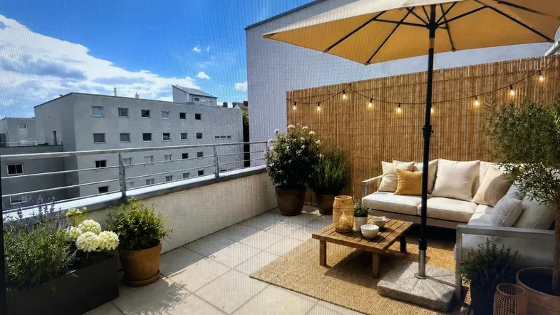 Gemütliche Dachterrasse mit Sitzbereich, Sonnenschirm und Blick auf die Stadt.