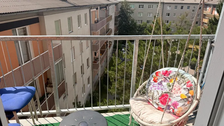 Gemütlicher Balkon mit Hängesessel, kleinem Tisch und Blick auf umliegende Wohngebäude.
