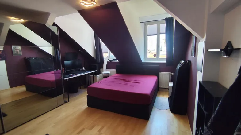 Gemütliches Schlafzimmer im Dachgeschoss mit Bett, Schreibtisch, Spiegelschrank und auffälliger lila-weißer Wandgestaltung.