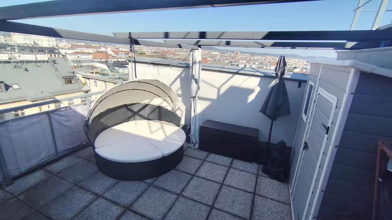 Geräumige Dachterrasse mit Liegemöbeln und weitem Blick über die Stadt an einem sonnigen Tag.