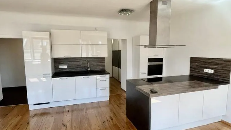 Moderne Küche mit weißen Hochglanzfronten, dunklen Arbeitsplatten und einer Kochinsel auf Holzboden.