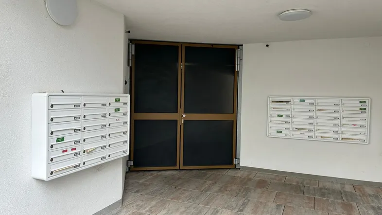 Eingangsbereich eines Mehrfamilienhauses mit Briefkästen und Zugangstür.