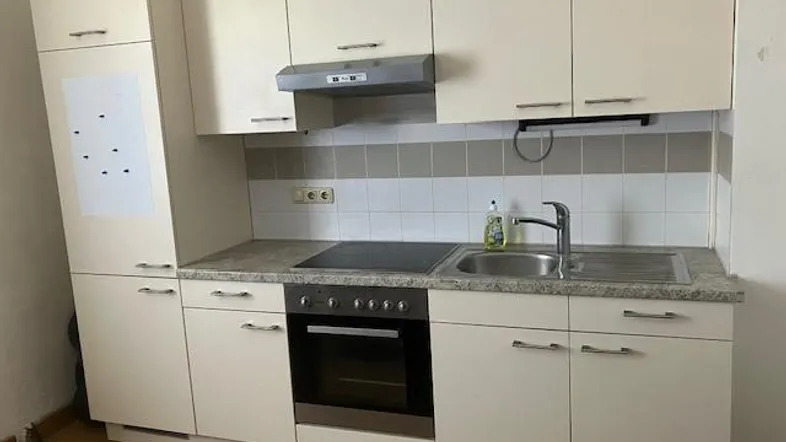 Moderne Einbauküche mit hellen Schränken, Herd, Spüle und Dunstabzugshaube.