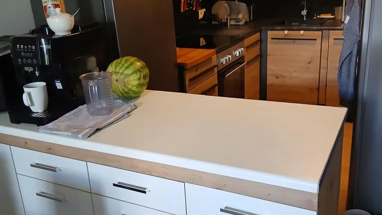 Moderne Küche mit Holzelementen, schwarzer Arbeitsplatte und weißer Kücheninsel, ausgestattet mit Kühlschrank und Kaffeemaschine.