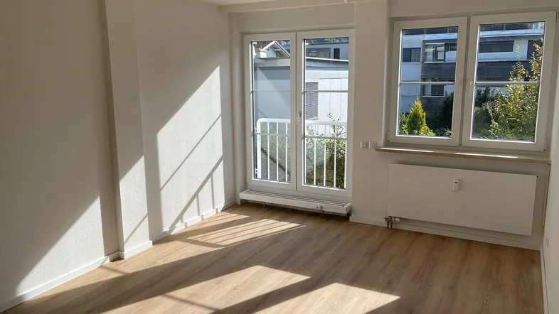 Helles Zimmer mit Laminatboden und Zugang zu einem französischen Balkon, durchflutet von Sonnenlicht.