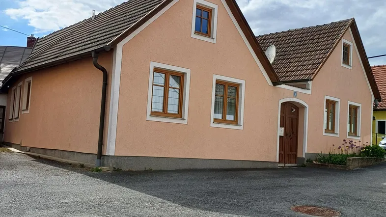 Zweistöckiges Wohnhaus mit hellrosa Fassade und braunem Dach unter bewölktem Himmel.