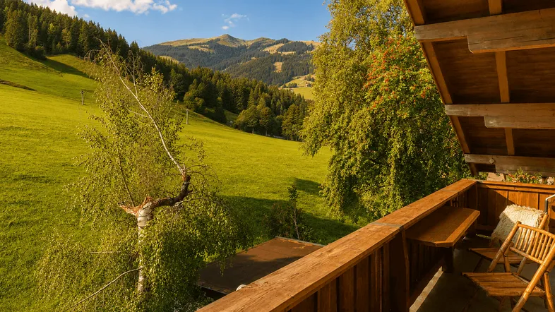 Balkon mit Holzboden und Geländer, bietet einen weiten Blick auf grüne Wiesen und Berge.