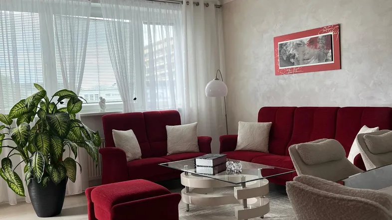 Helles Wohnzimmer mit roten Sofas, einem Couchtisch aus Glas und Fliesenboden.