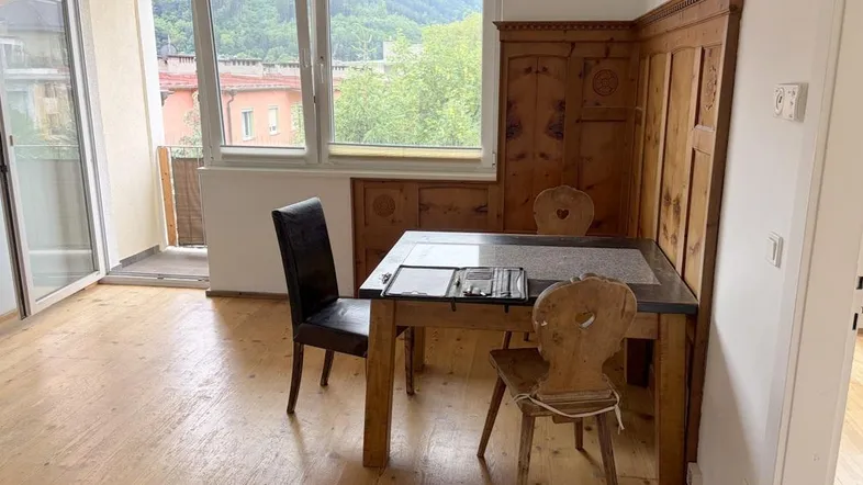 Heller Wohn-Essbereich mit Holzboden, traditioneller Holzvertäfelung und Zugang zum Balkon mit Bergblick.